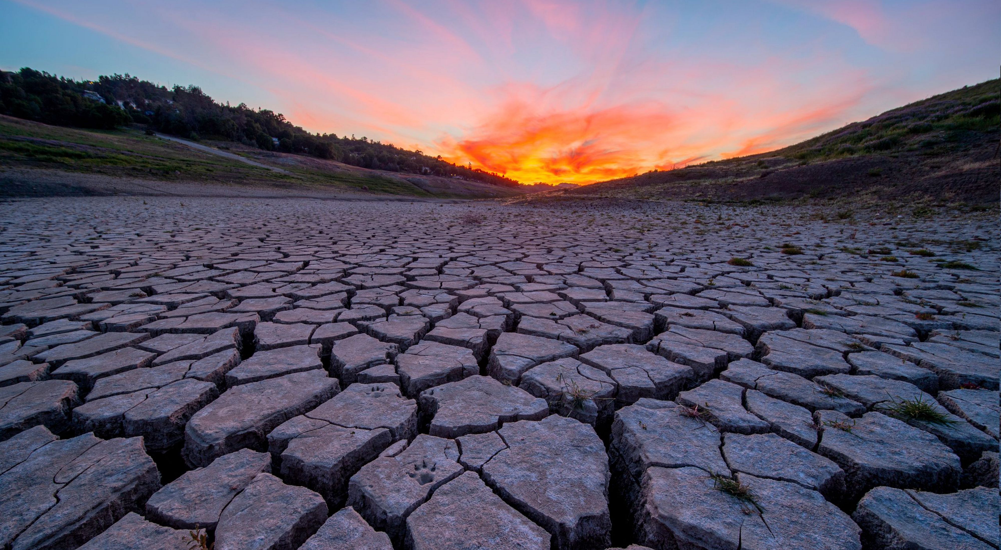 Photo of an orange sunset across a parched, cracked riverbed.