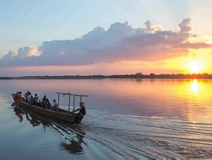 boat ferries people across river with ripples at sunset