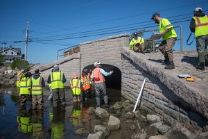 A group of people in safety vests inspect a new bridge over a stream.