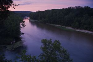 A purple and pink sunsest over a forested river landscape.