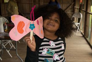 A little girl holds up a pink butterfly made of construction paper.
