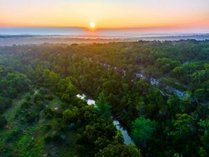 The sun rises over a vast expanse of green brush and a blue river.