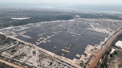 An aerial photo features thousands of solar panels in tight straight rows on flat dry terrain in India.
