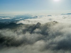 Aerial view of a vast fog-shrouded landscape with mountains and lakes.