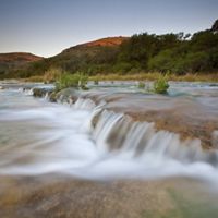 Photo taken at low-speed of a river flowing over tan rocks.