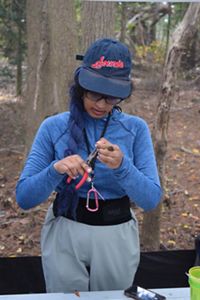 A woman stands and measures a small bird that she holds in her hands.