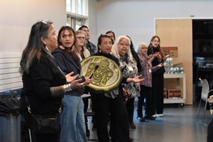 : Tlingit First Nation members playing a drum and singing with palms facing up.