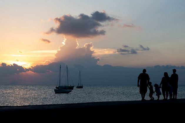 Familia a contraluz caminando por la orilla de la playa al atardecer. 