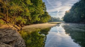 A river flows calmly past a sandy beach surrounded by a green forest.