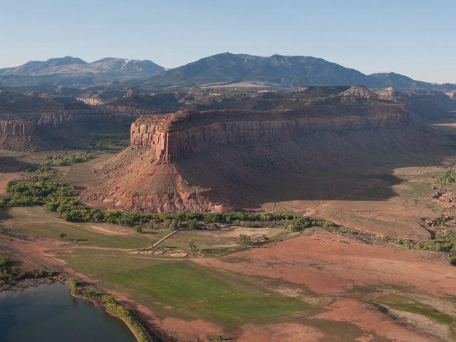 Landscape seen from above: layered mountains in distance, green and brown low land with few trees in foreground.