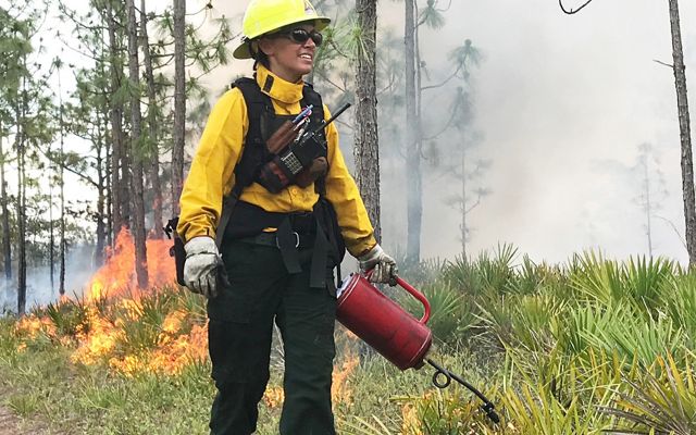 Woman holding a drip torch preparing to start a prescribed fire. 