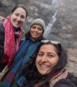 Three women standing in front of a waterfall.