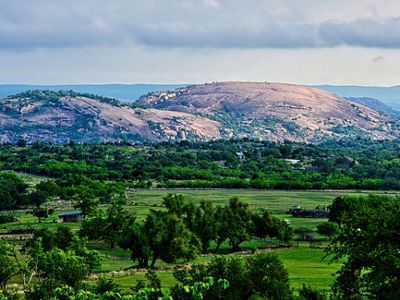 A towering granite hill overlooks green fields.