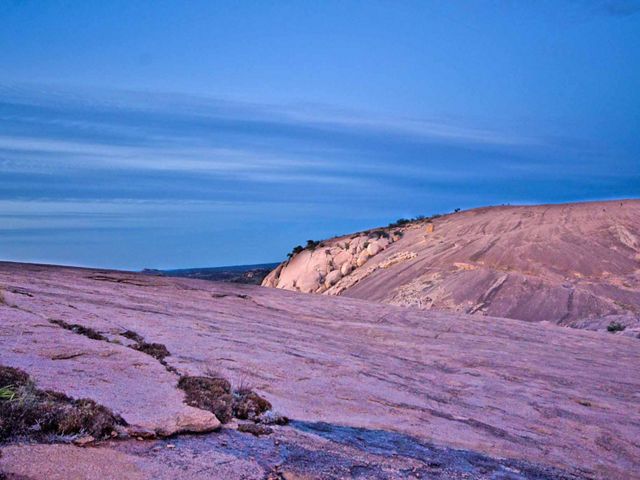 Pink colored rocks dotted with green shrubs at sunset.