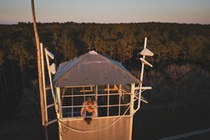 Man stands in fire tower overlooking a forest. 