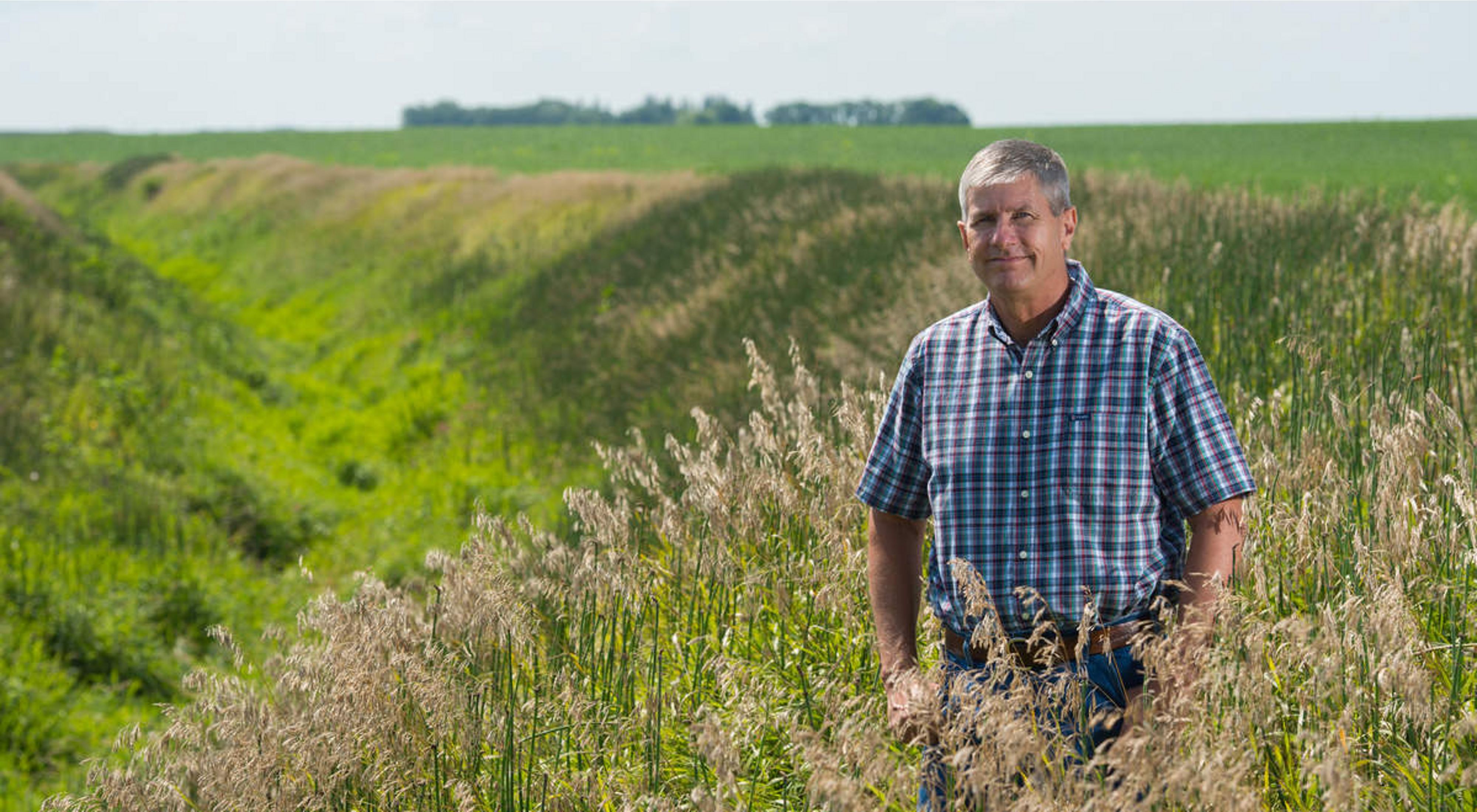 A man in blue plaid shirt standing in an agricultural field.
