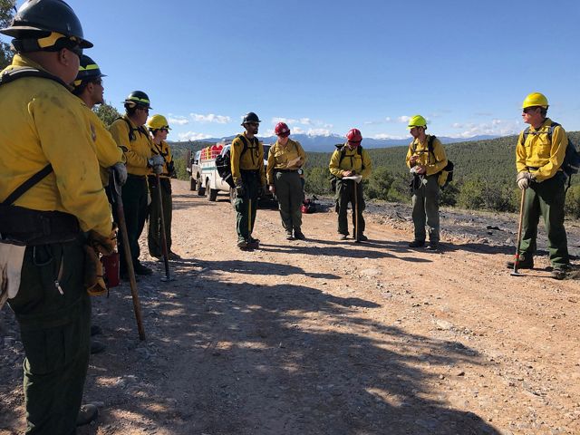 A group of men in yellow burn suits listen to instructions.
