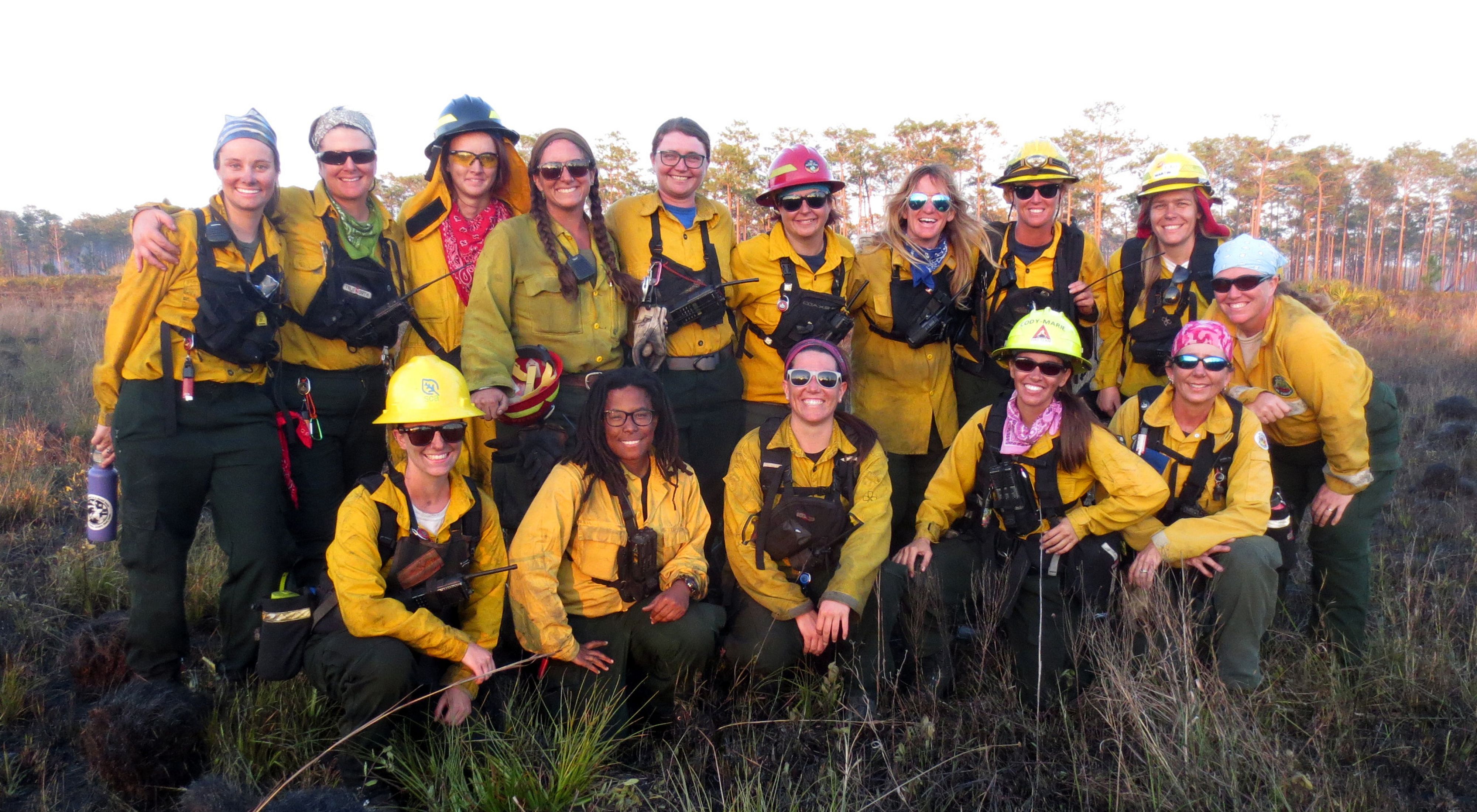A group of about 15 smiling women in fire gear.