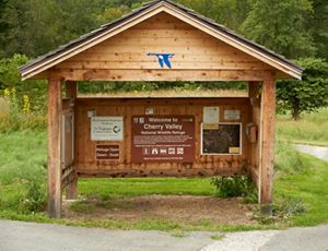 A covered wooden kiosk with a sign that reads Welcome to Cherry Valley; the interior wall has visitor information posted on it.
