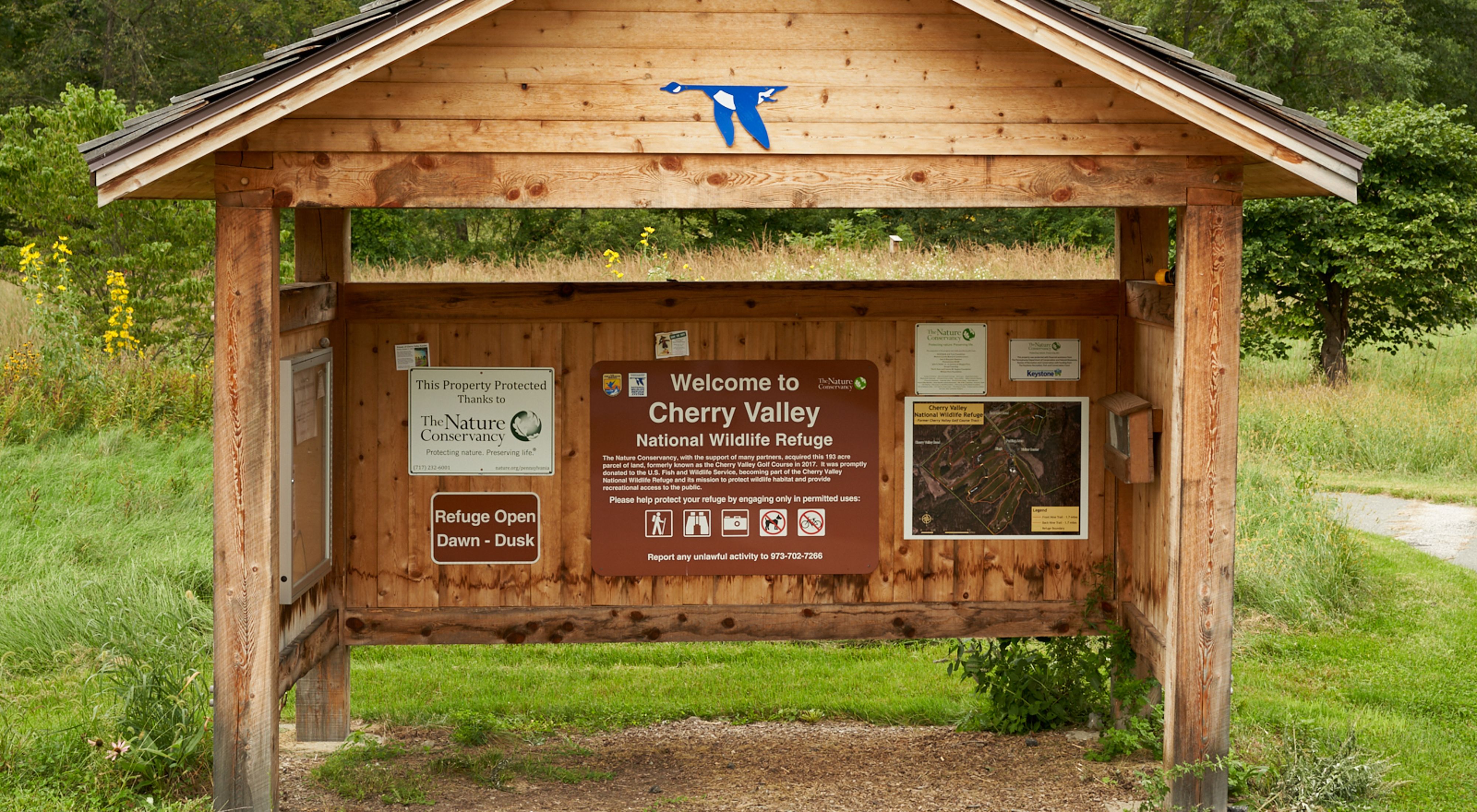 A wooden kiosk welcome visitors to Cherry Valley. The interior wall of the covered kiosk is covered with signs and maps providing visitor information.