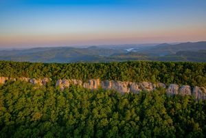 Aerial view of a forest-covered rock ridge with mountains in the distance.