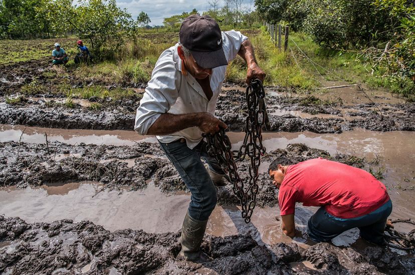 Edilson Ortiz Arango uses towing chains to extract his tractor from deep mud
