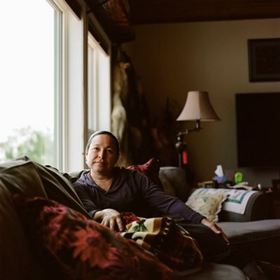 woman sits on couch by window amid pillows, looks at camera