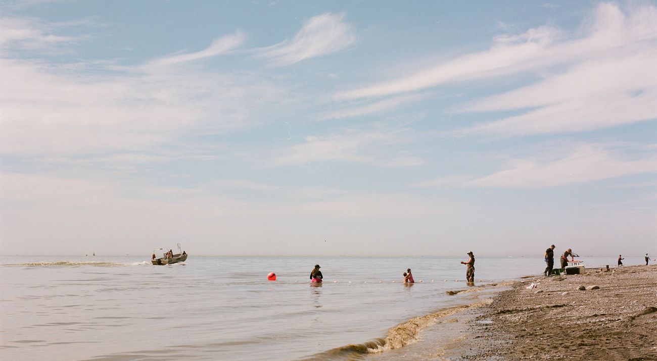 family on rocky beach with net stretched on buoys. boat in instance leaving shore