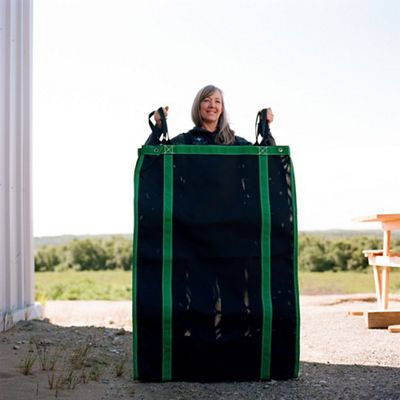 Woman stands on sunny day holding large black net bag that is several times wider than her and nearly as tall as her