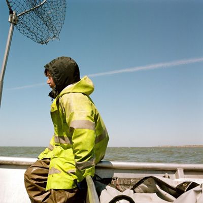 a boy in a yellow fishing coat sit on the edge of a boat in the water with a net nearby