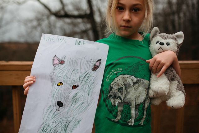 Una niña sostiene un lobo de peluche en un brazo y un dibujo de un lobo en el otro.