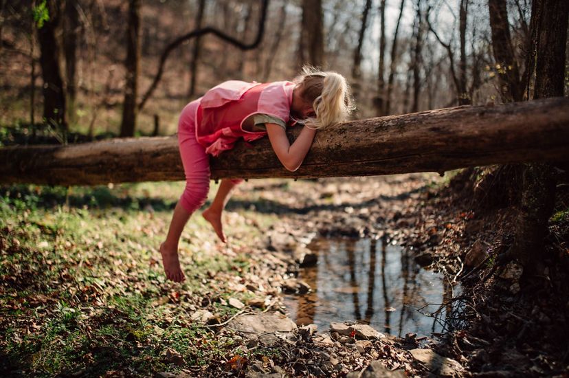 Una niña yace boca abajo en un tronco sobre un arroyo.