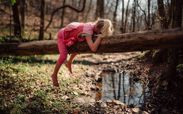 Una niña yace boca abajo en un tronco sobre un arroyo.