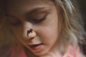 Closeup of a girl with a tadpole on her nose.