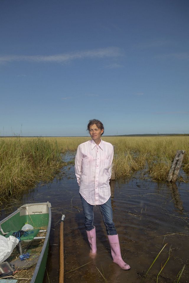 A woman stands next to a canoe in pink boots.