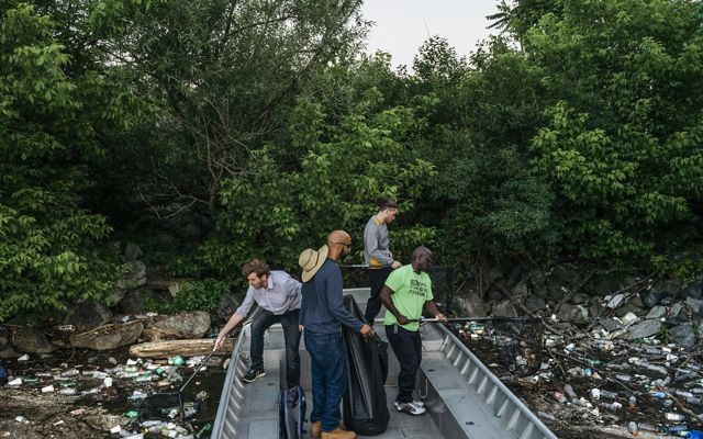 Four men scoop trash from the river's surface with nets.
