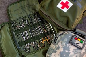 Army green medical kit is opened flat with scissors and pinchers displayed