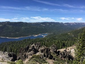 View from a high overlook looking down at slopes covered in dense forests and a body of water in a valley.