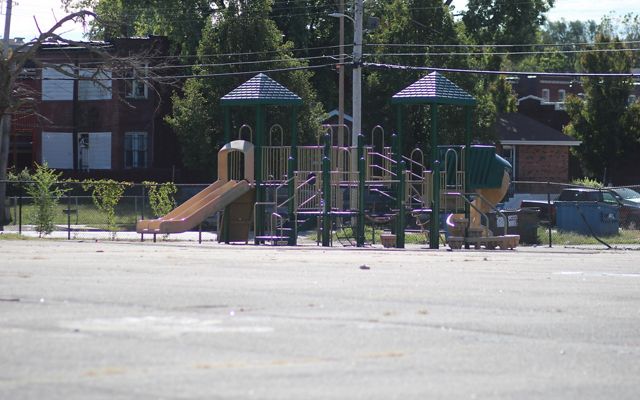 A play structure sits on a large paved schoolyard.