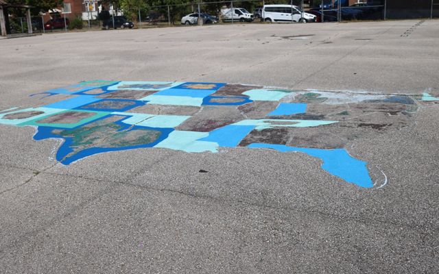 An outline of the United States map is painted on a paved schoolyard.