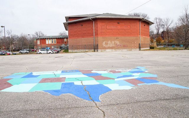 A large paved schoolyard with a map of the U.S. painted on it in front of a red-brick building.