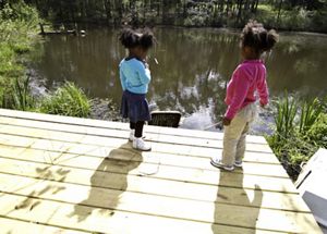 2 toddlers stand on a dock and look out over a creek on a spring day.