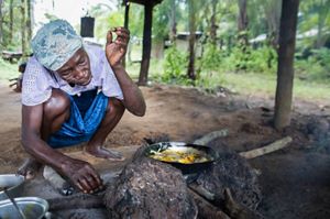 Woman crouches next to cooking fish