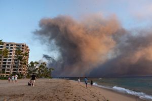 Wildfire smoke moving over a beach with a big building on the left side of the image.