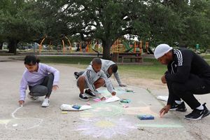 Three children and one adult draw with chalk on a concrete path in a park.
