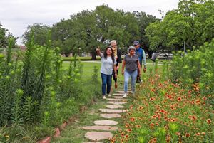 Personas caminan en un jardín con flores y arbustos abundantes.