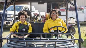 Two TNC Globe Interns dressed in yellow protective fire gear sit in a UTV in front of a fire engine, before a prescribed burn at Sandyland Sanctuary.