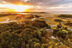 Aerial view of Brownsville Preserve. An historic brick home with a circular oyster shell driveway stands in a clearing between thick stands of trees. In the background the sun rises over the Atlantic.