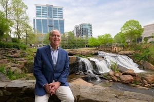 Greenville Mayor Knox white sits on a rock in a riverfront park.