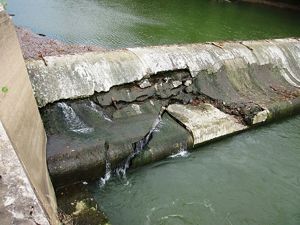 Concrete dam with cracks and areas that are crumbling.